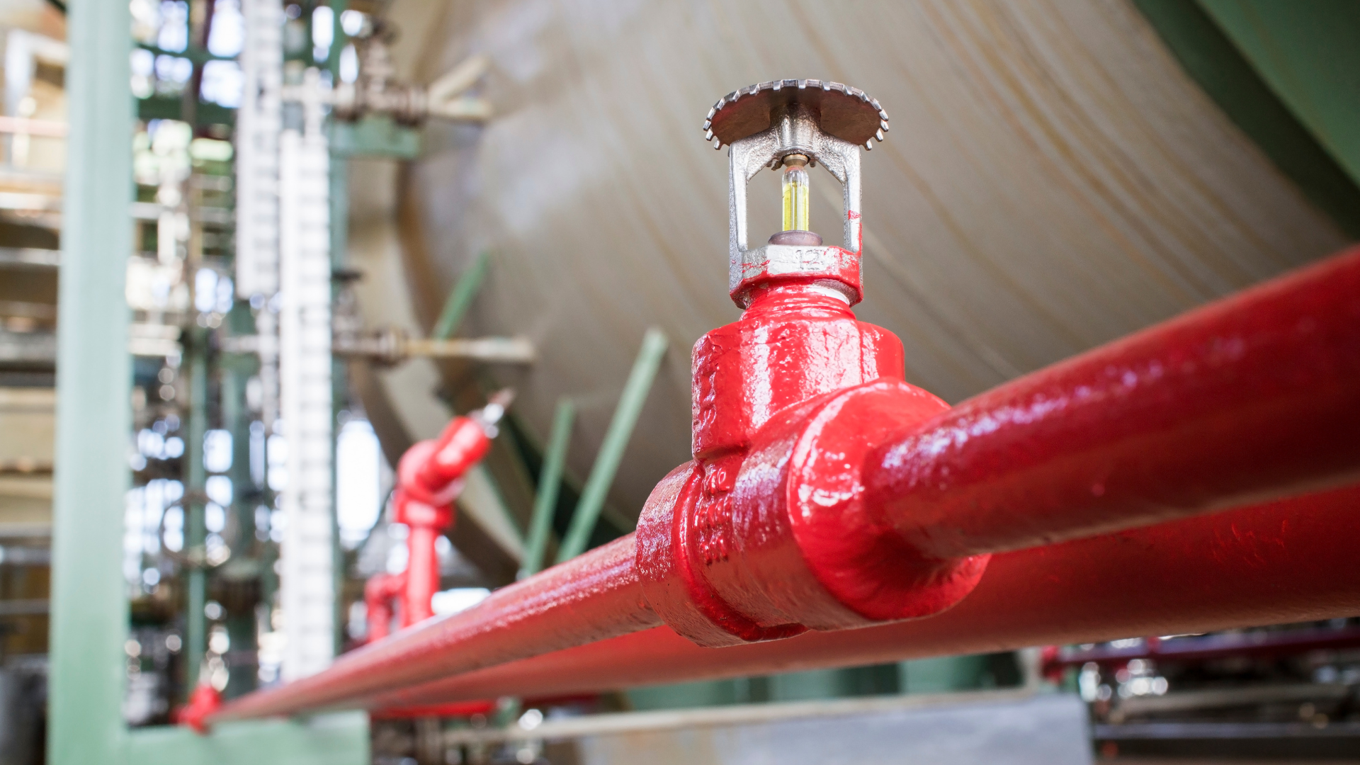 A fire sprinkler is hanging from a red pipe in a factory.