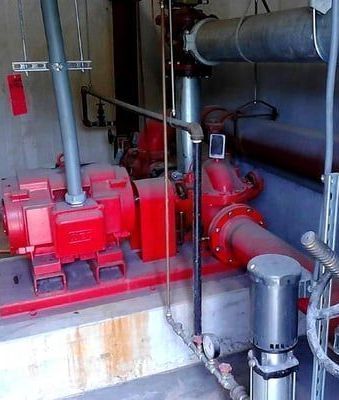 A room with a lot of pipes and a red pump.
