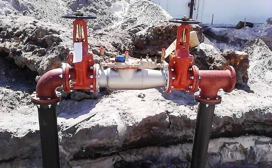 Two red pipes are connected to each other on a rocky surface.