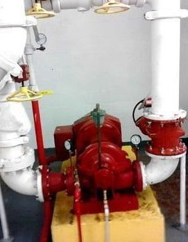 A red fire pump is sitting on top of a yellow block next to white pipes.