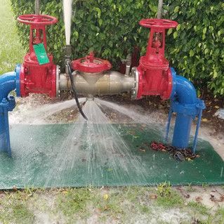 A red valve is spraying water from a blue pipe.