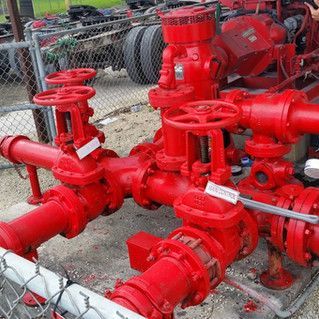 A bunch of red pipes and valves are sitting next to a chain link fence.