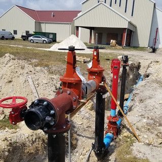 A bunch of pipes are sitting in the dirt in front of a building.