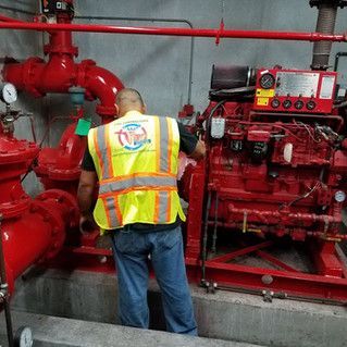 A man in a yellow vest is working on a fire pump.