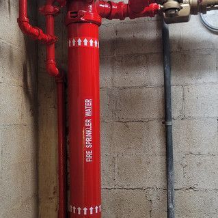 A red fire sprinkler water pipe is attached to a brick wall.
