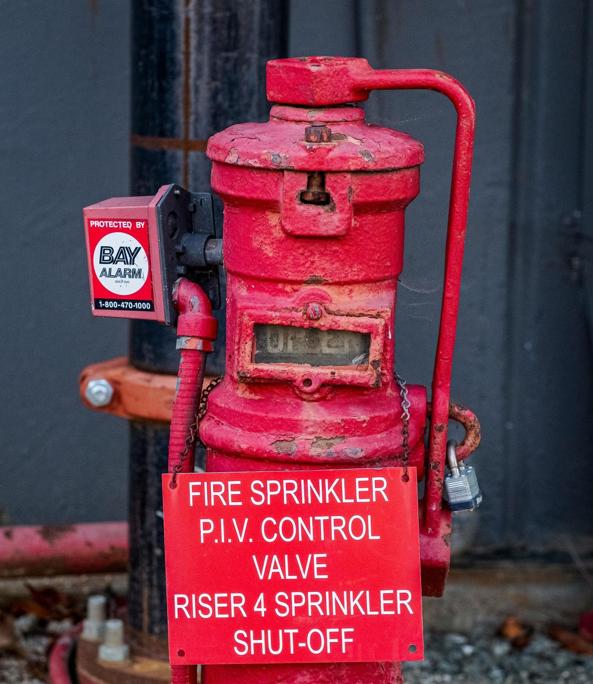 A red fire sprinkler with a sign that says fire sprinkler p.i.v. control valve