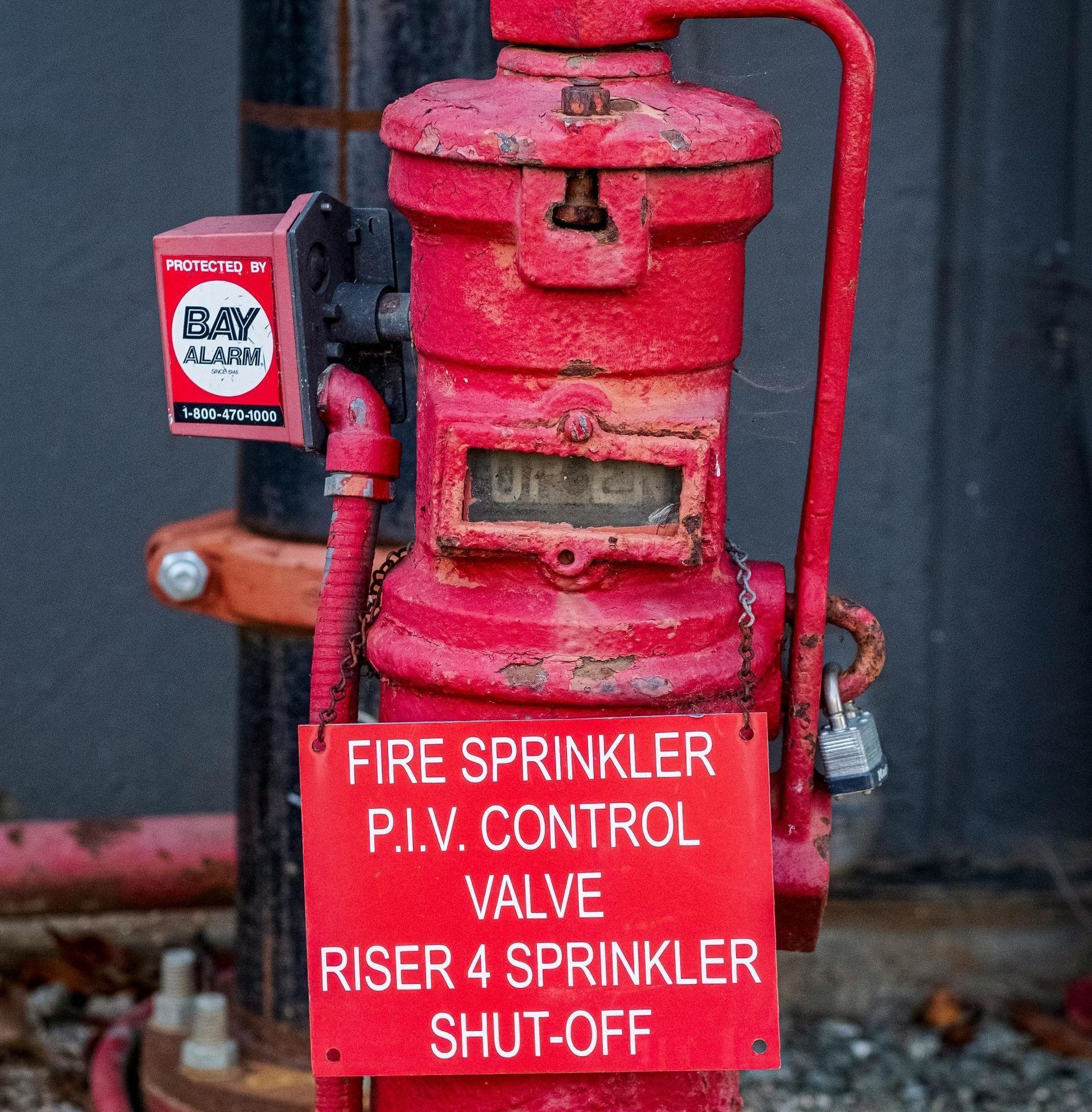 A red fire hydrant with a sign that says fire sprinkler p.i.v. control valve riser 4 sprinkler shut off