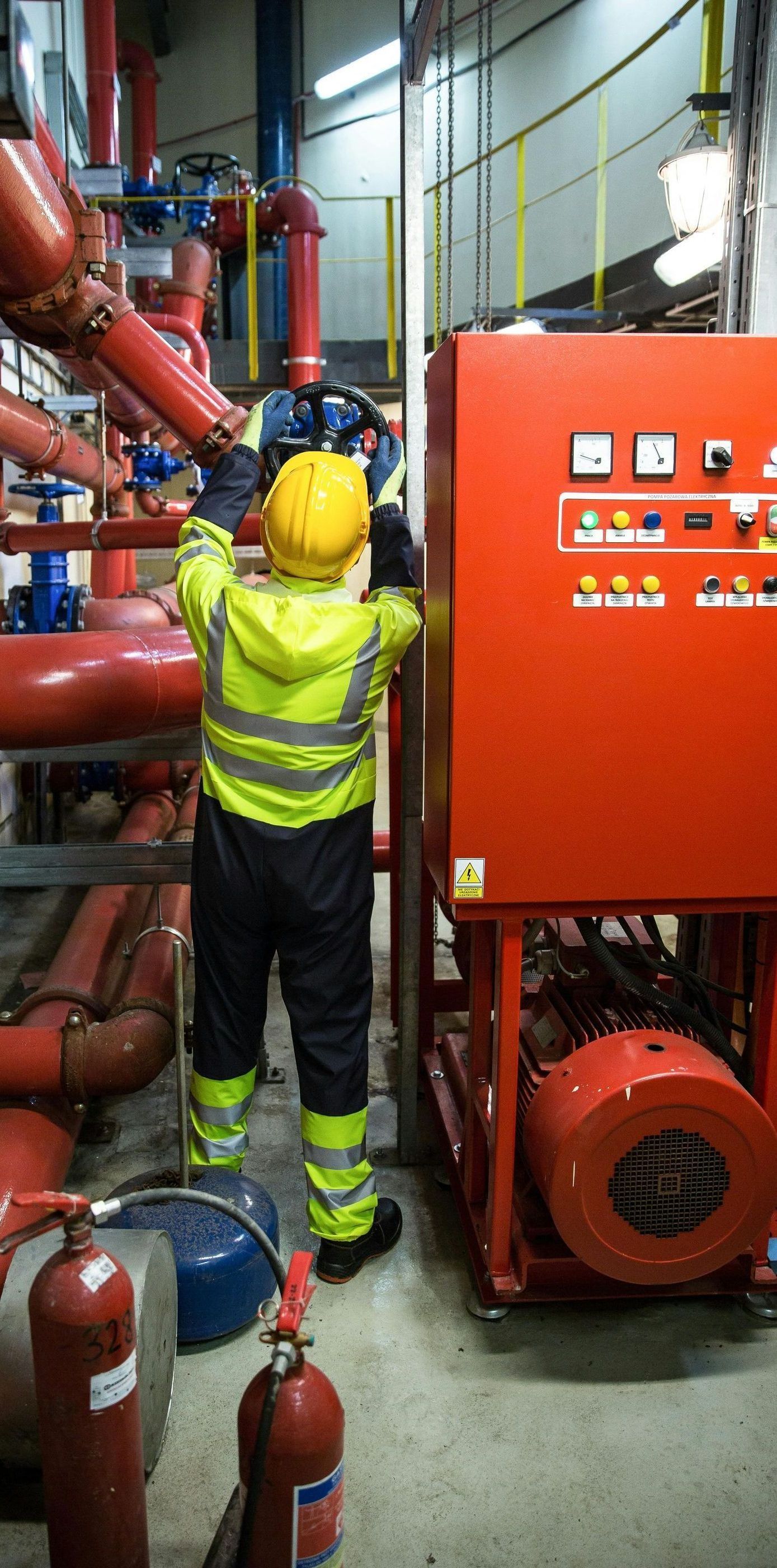 A man in a yellow hard hat is working on a machine in a factory.
