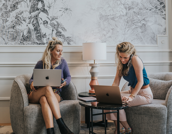 Sarah Glasbergen en Maaike zitten in stoelen en gebruiken laptops.
