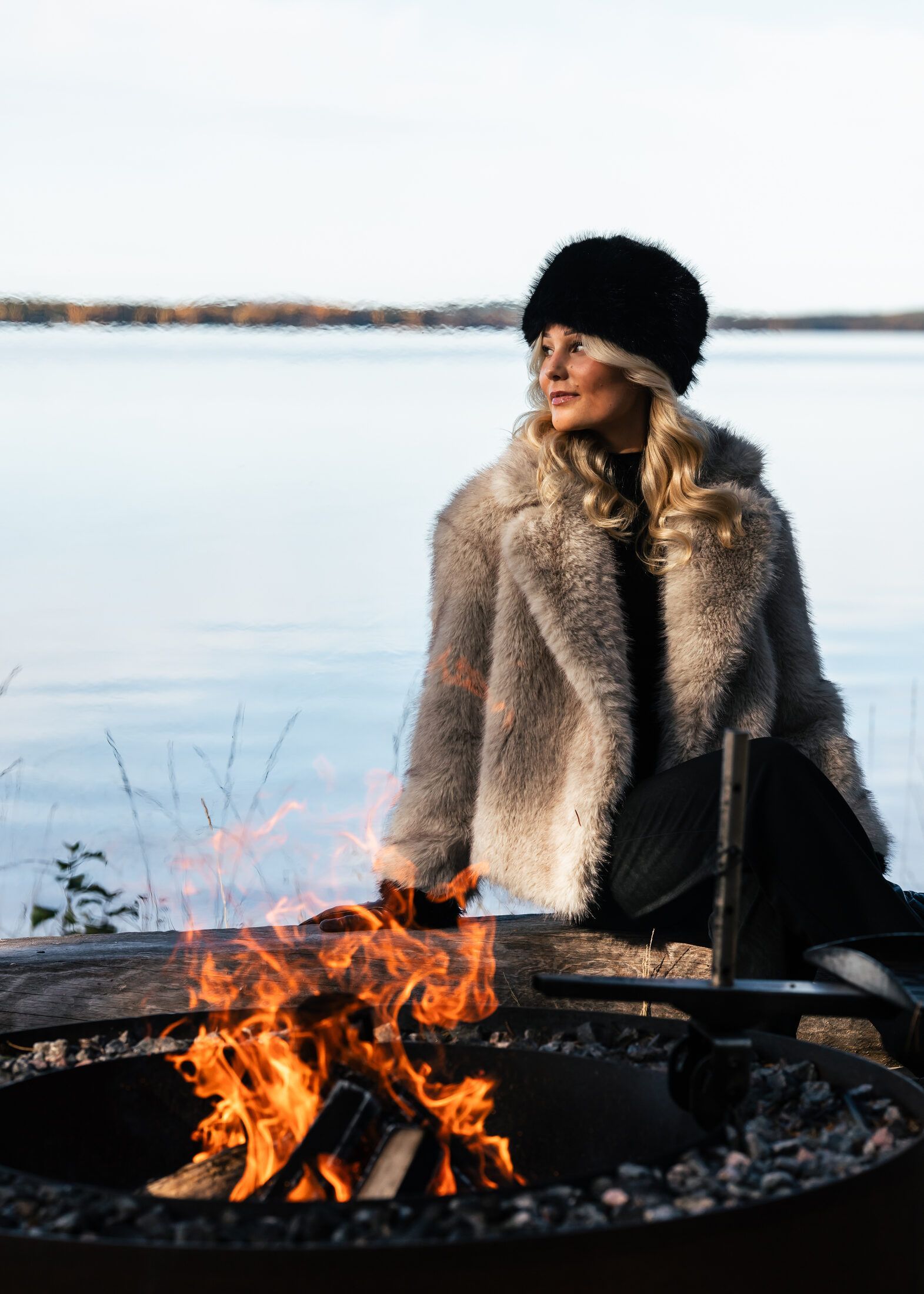 Guest sitting by a fire pit on a lake shore in Lapland in autumn