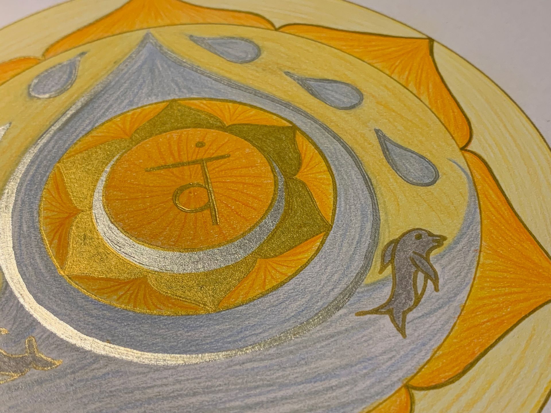 Yellow and silver chakra mandala with dolphin, teardrops, and Sanskrit symbol.