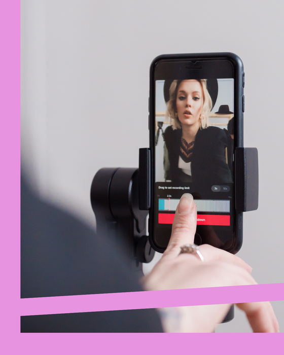Hand using a phone on a selfie rig, showing a portrait video with editing controls on screen