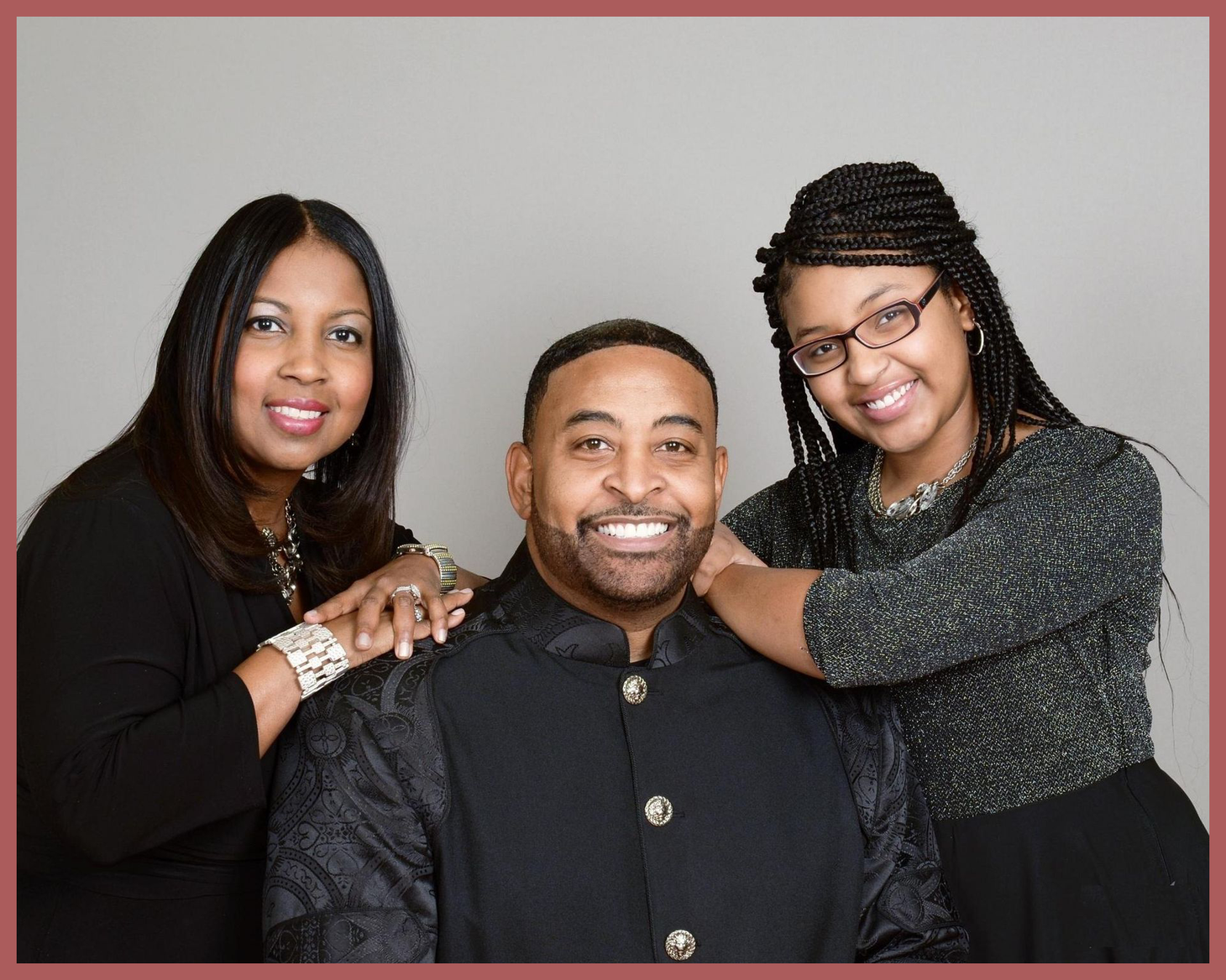 Three smiling adults posing together against a gray backdrop, framed by a red border.