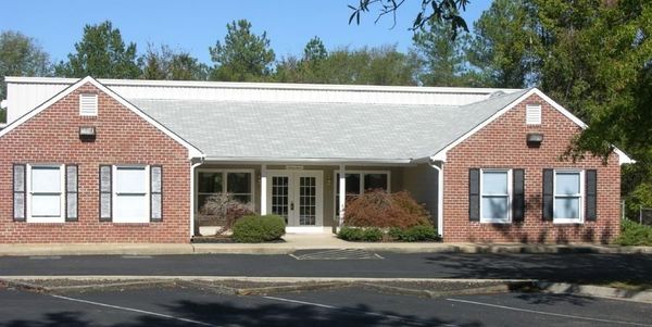 Brick office building with white roof, black shutters, and a central glass entrance surrounded by shrubs.