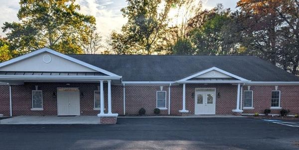 Brick one-story commercial building with two white porticos and a dark parking lot in front