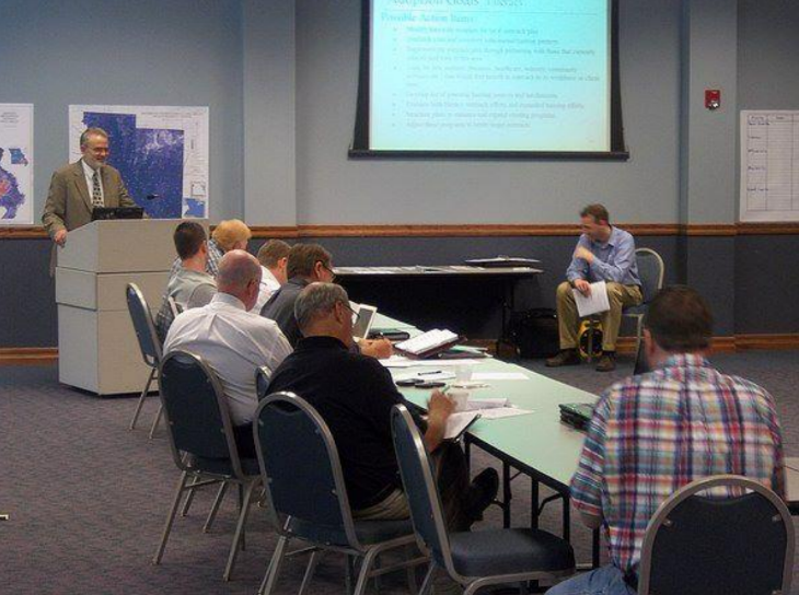 A man stands at a podium giving a presentation to a group of people