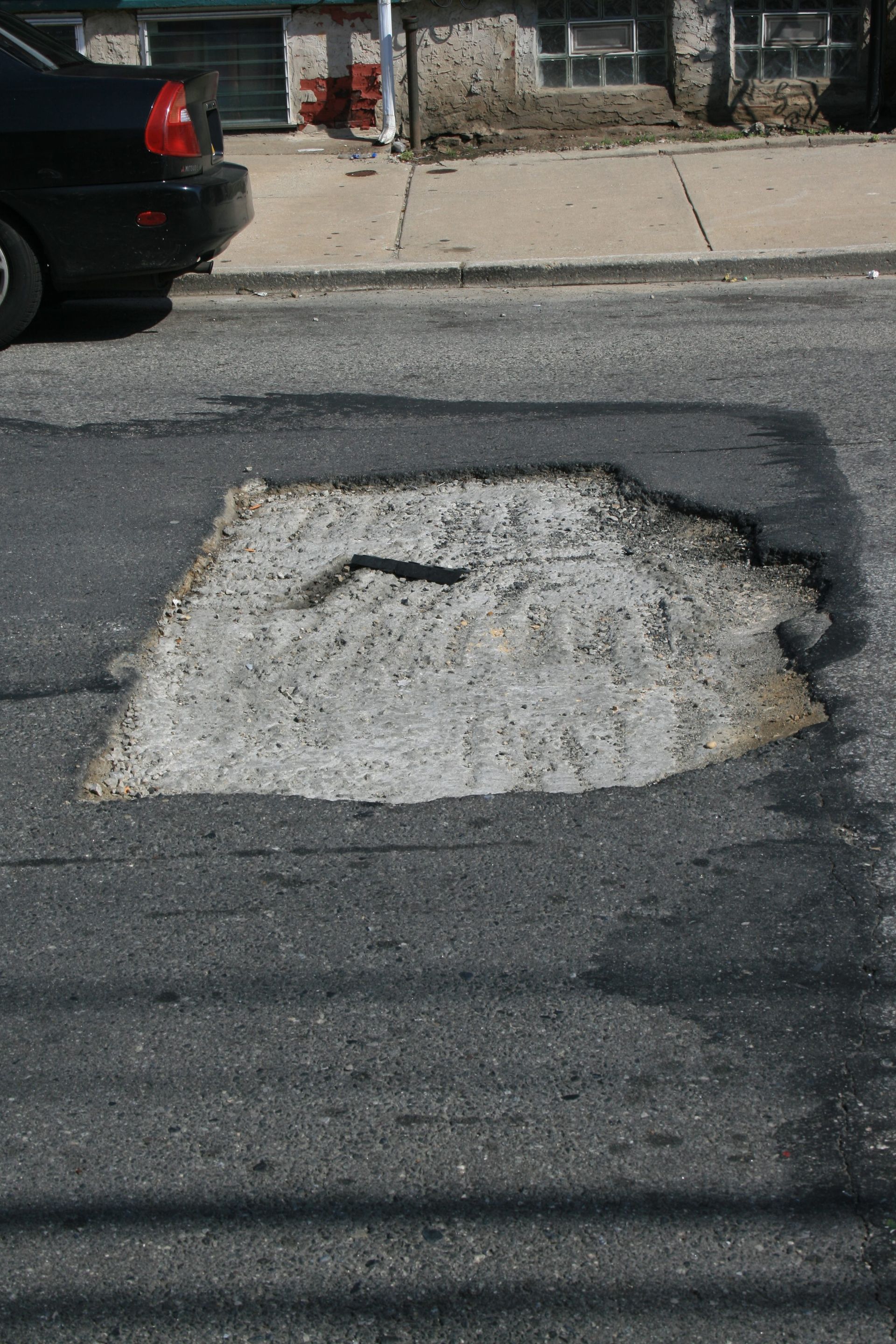A car is parked in front of a large hole in the road