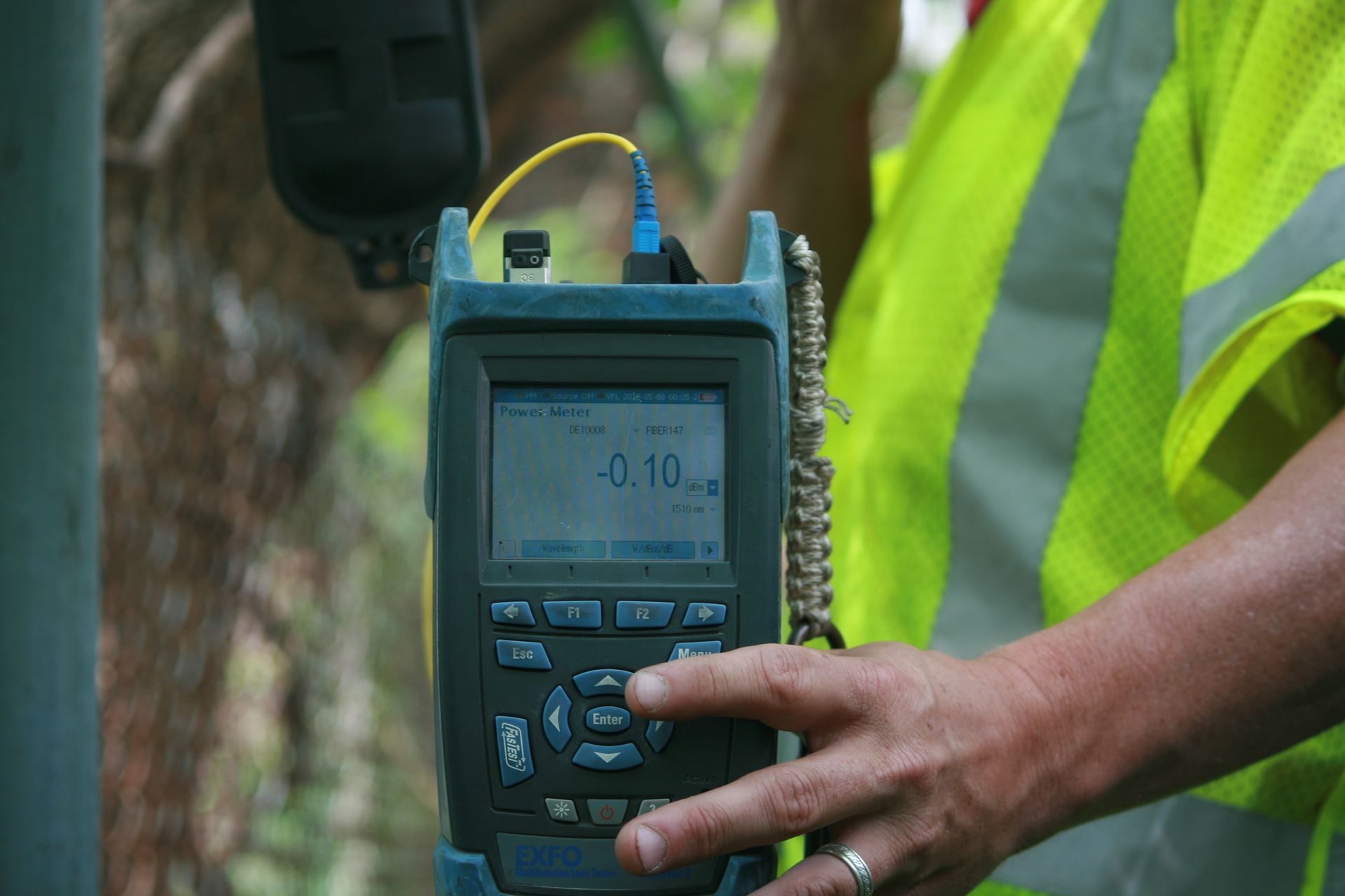 A man in a yellow vest is holding a device in his hand.