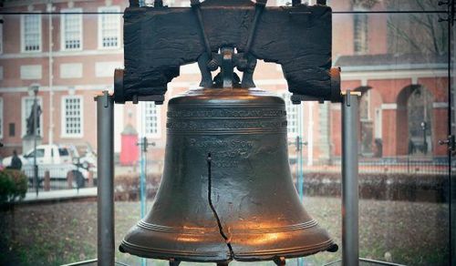 A large bell is hanging from a pole in front of a building.