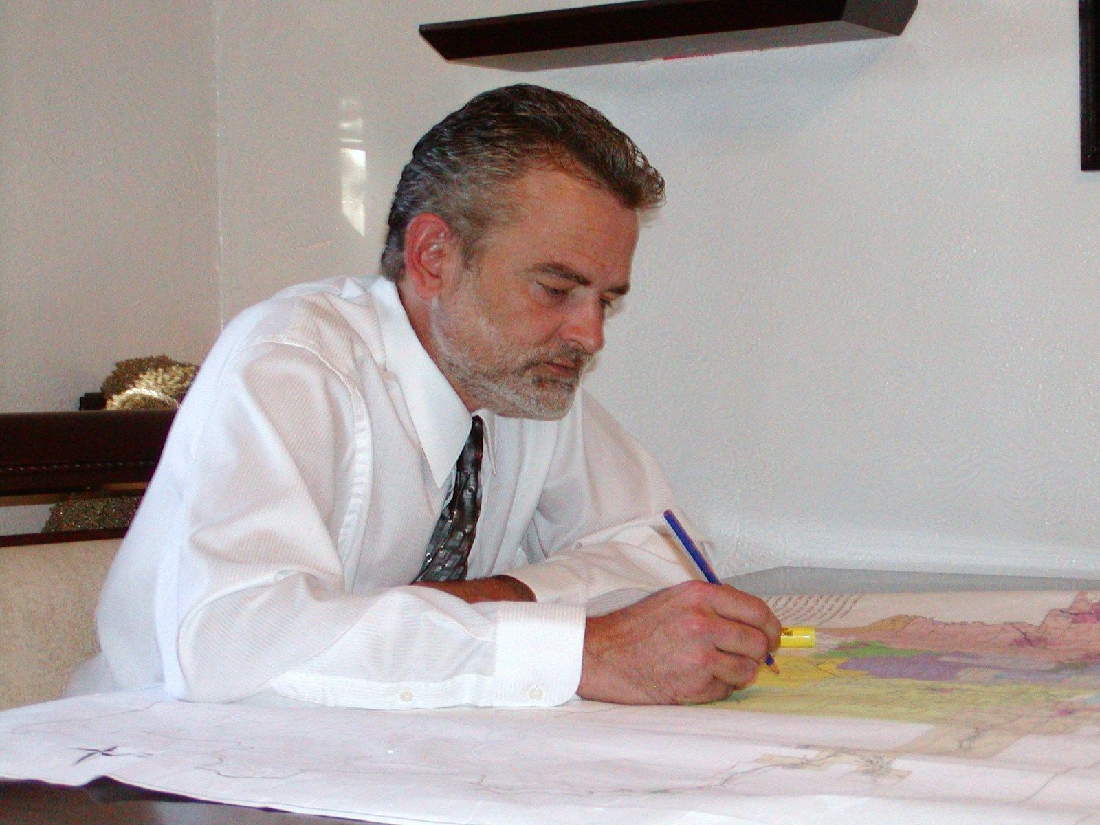 A man in a white shirt and tie is writing on a piece of paper