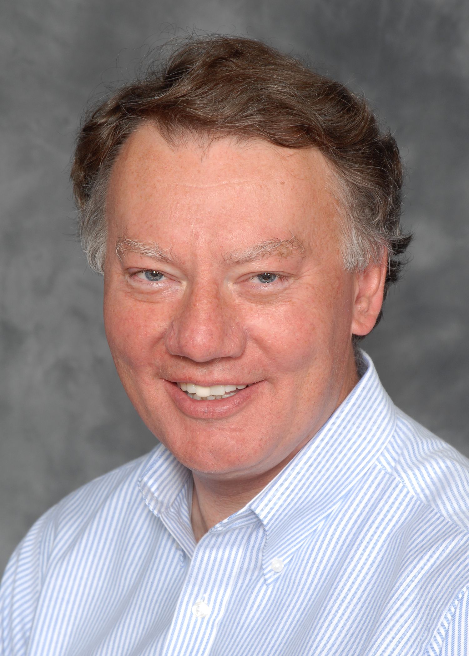 Thomas G. Robinson in a blue and white striped shirt is smiling for the camera.