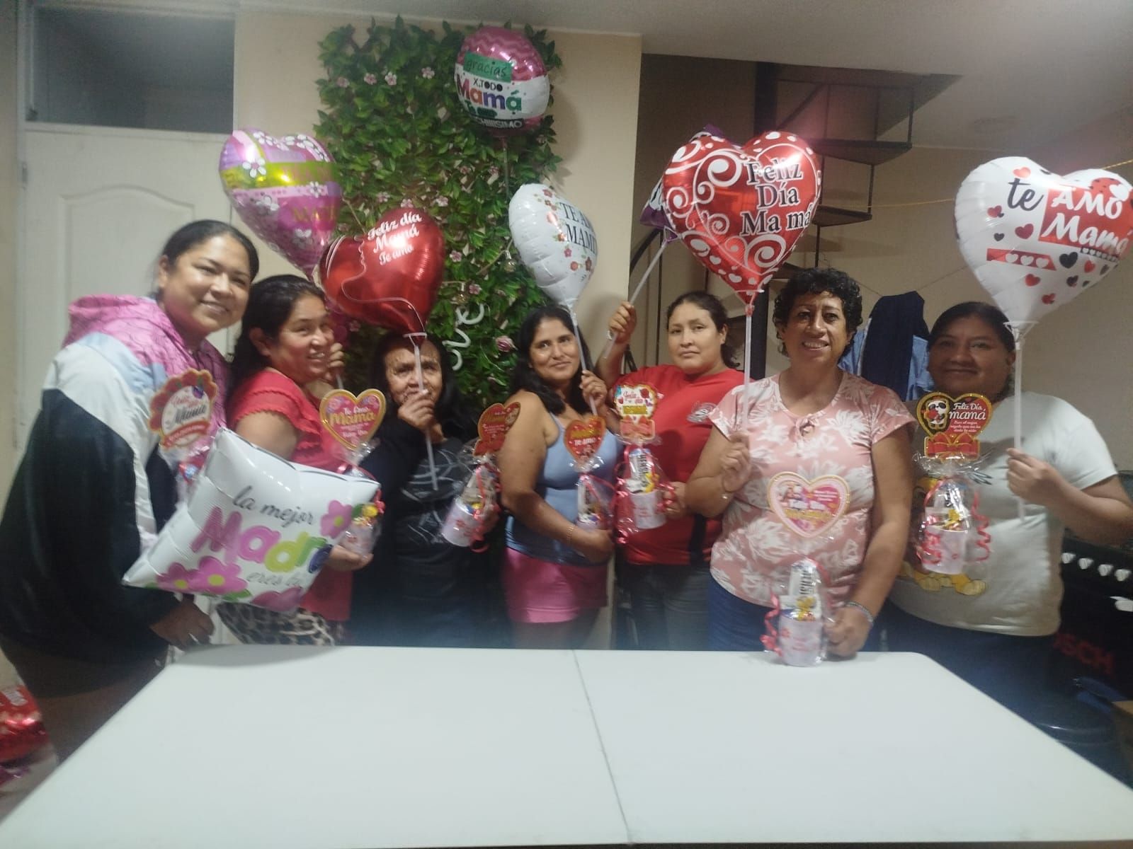 Grupo de personas posando en interiores con globos en forma de corazón y flores alrededor de un centro de mesa decorado.