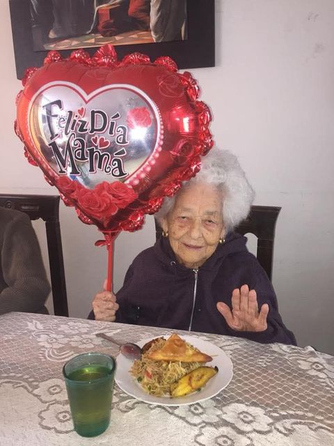 Una anciana sentada a una mesa sostiene un globo rojo