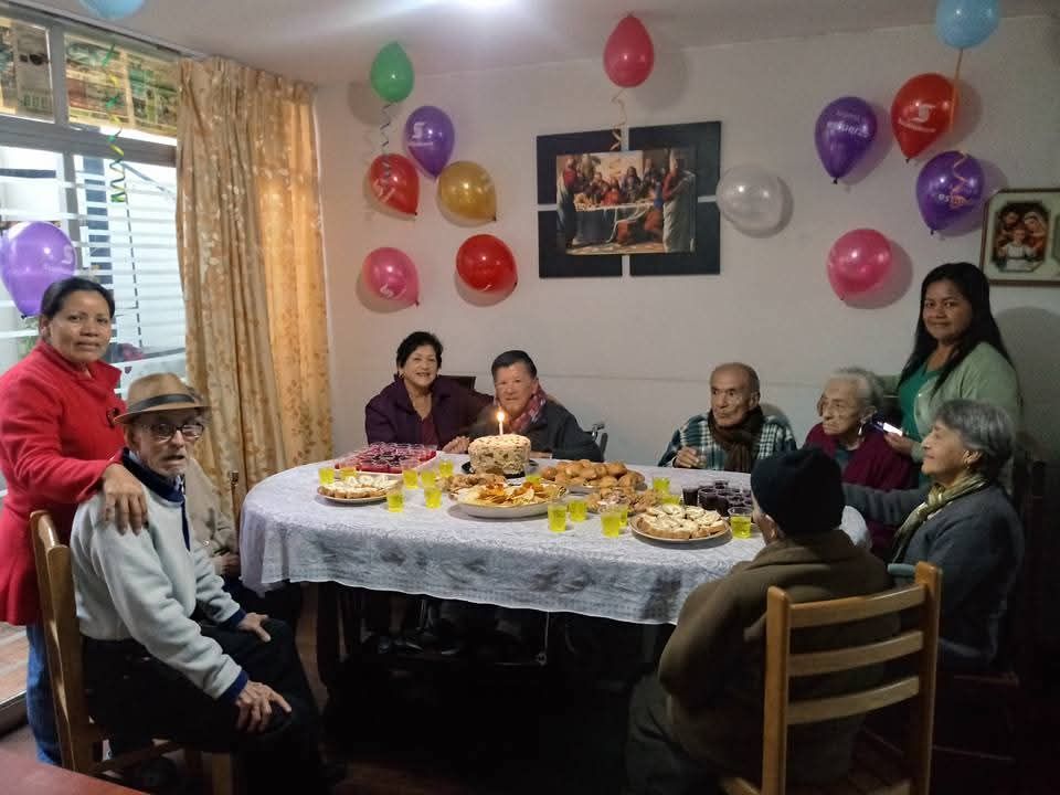 La gente se reunió alrededor de una mesa con comida y globos, celebrando en una sala de estar decorada.