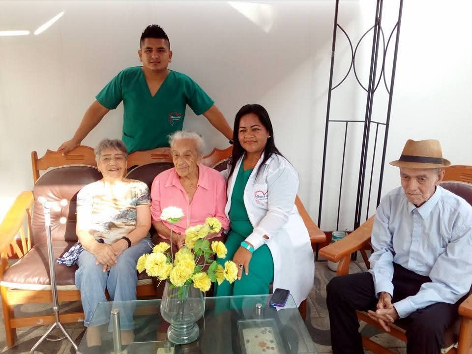 Cinco personas posando en un sofá en una habitación luminosa, con flores sobre la mesa y una persona con bata blanca.