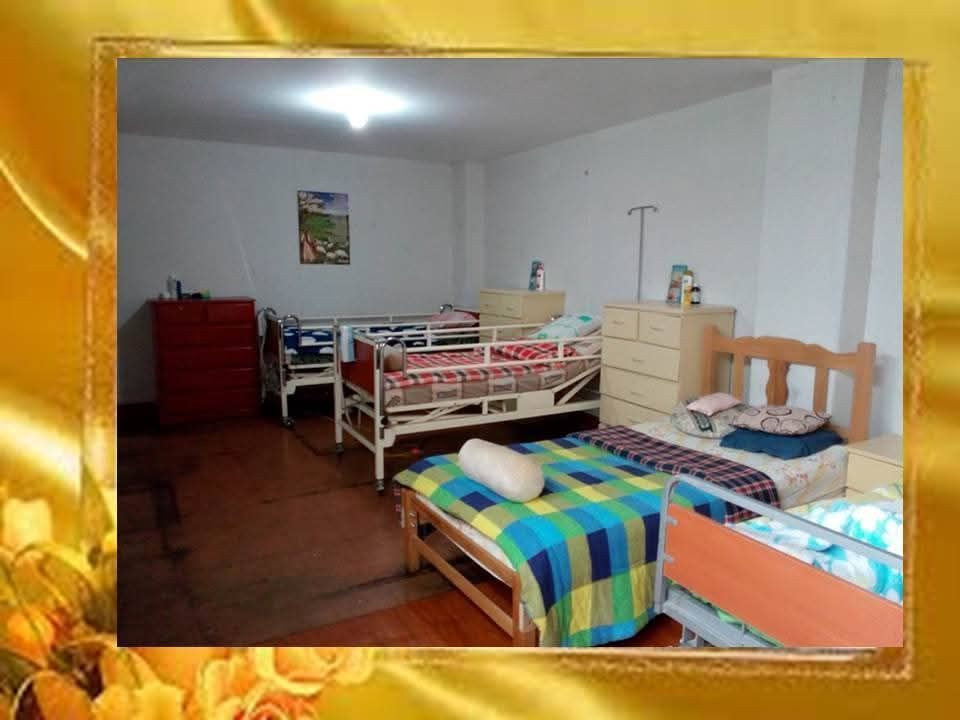 Habitación compartida con varias camas, mantas de colores y cómodas en una sencilla habitación tipo residencia estudiantil.