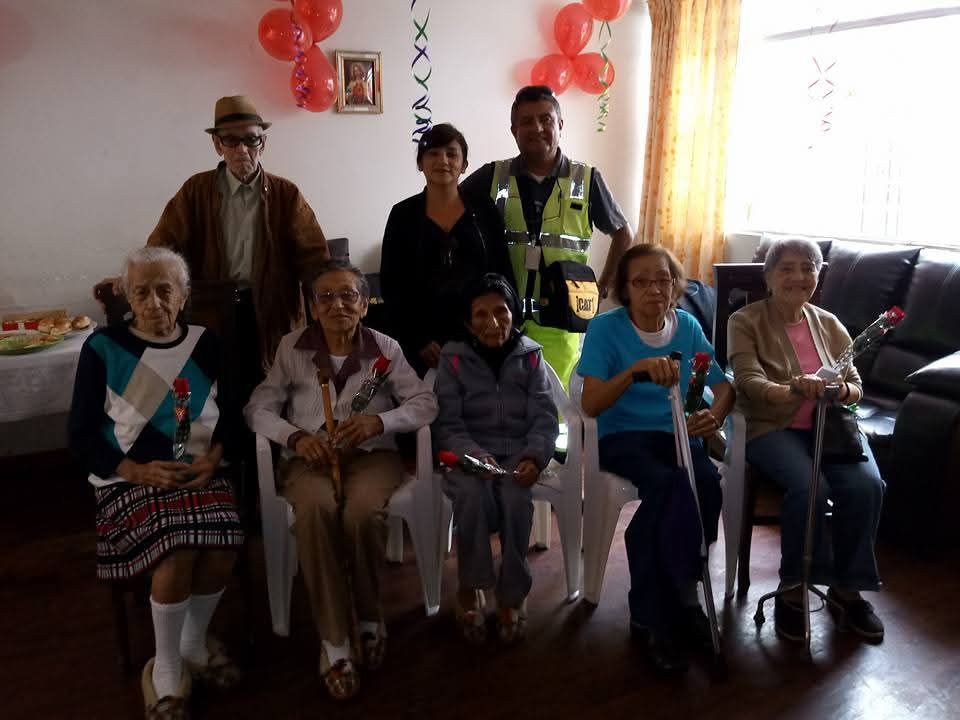 Grupo de personas sentadas y de pie en el interior de una habitación decorada con globos rojos y blancos.