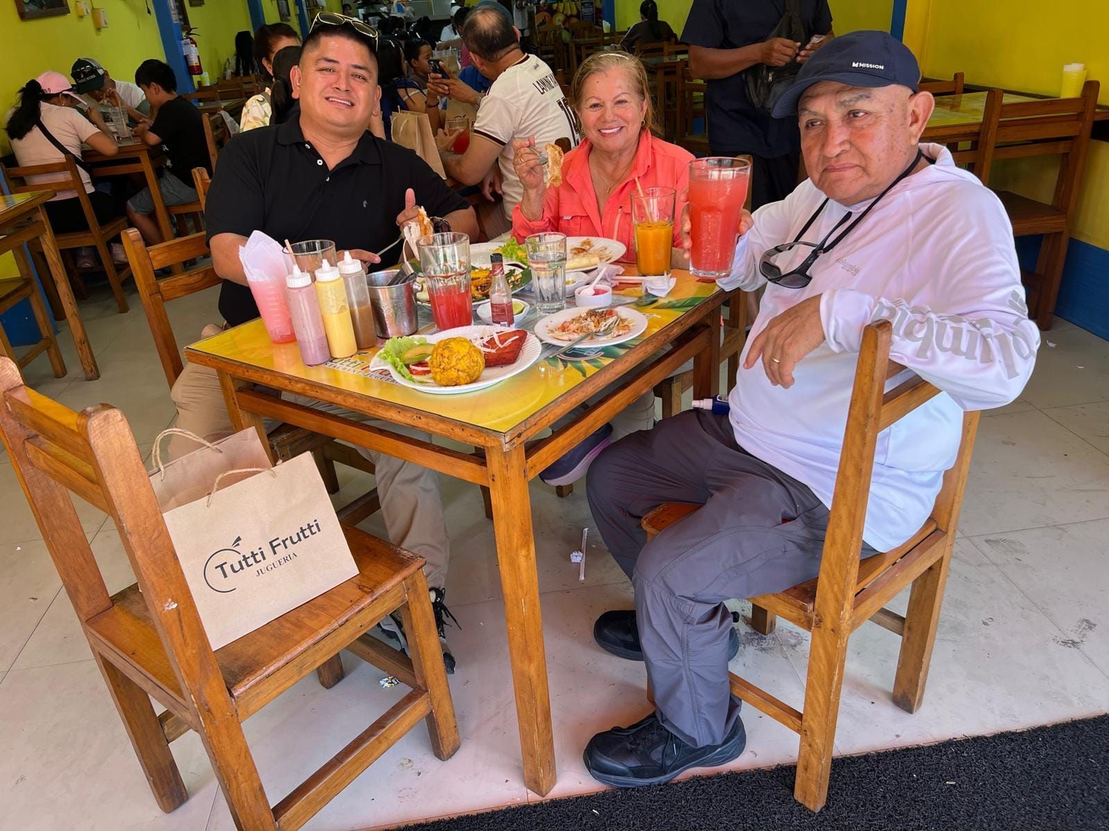 Tres personas sentadas en una mesa con bebidas y comida en un restaurante informal.