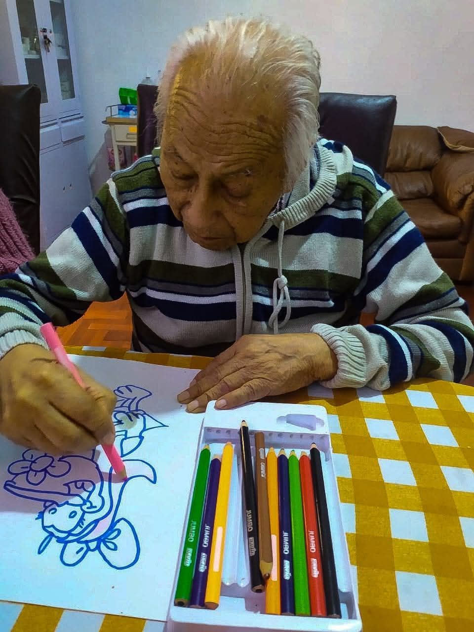 Persona coloreando con lápices en una mesa a cuadros en el interior de una vivienda.