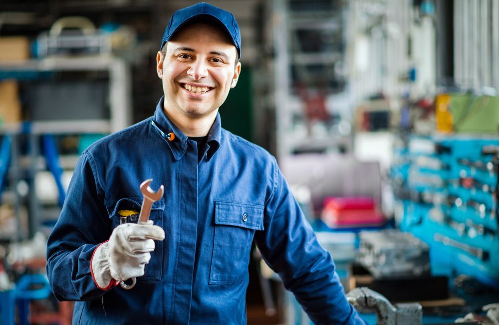 A Smiling Mechanic Is Holding A Wrench And A Flashlight In A Garage — Too Ezy Auto Electrics In Townsville, QLD