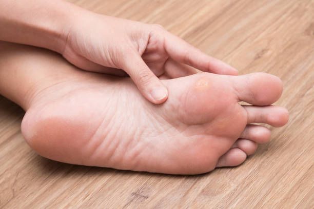A person is holding their foot on a wooden floor.