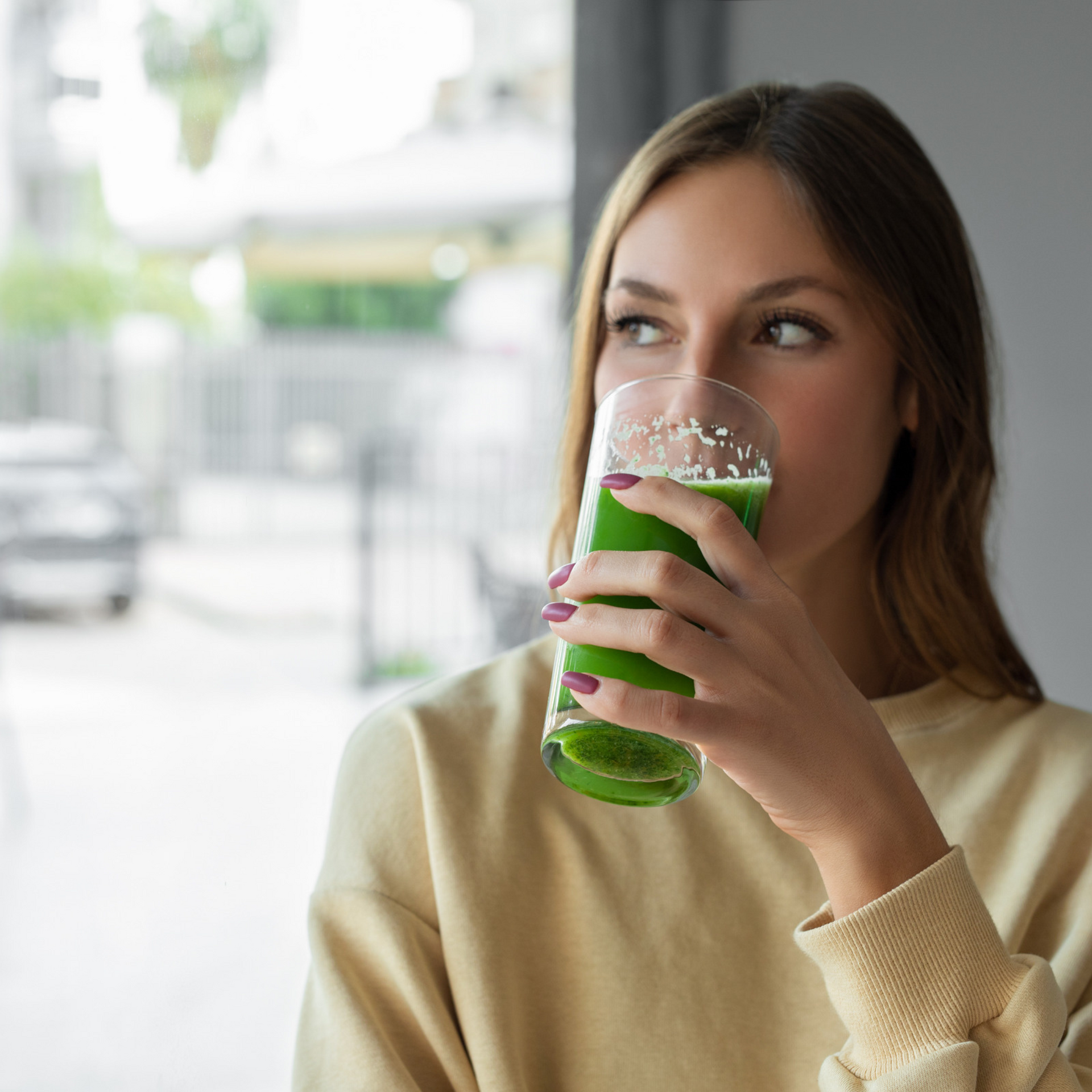 A woman is drinking a green smoothie from a glass.