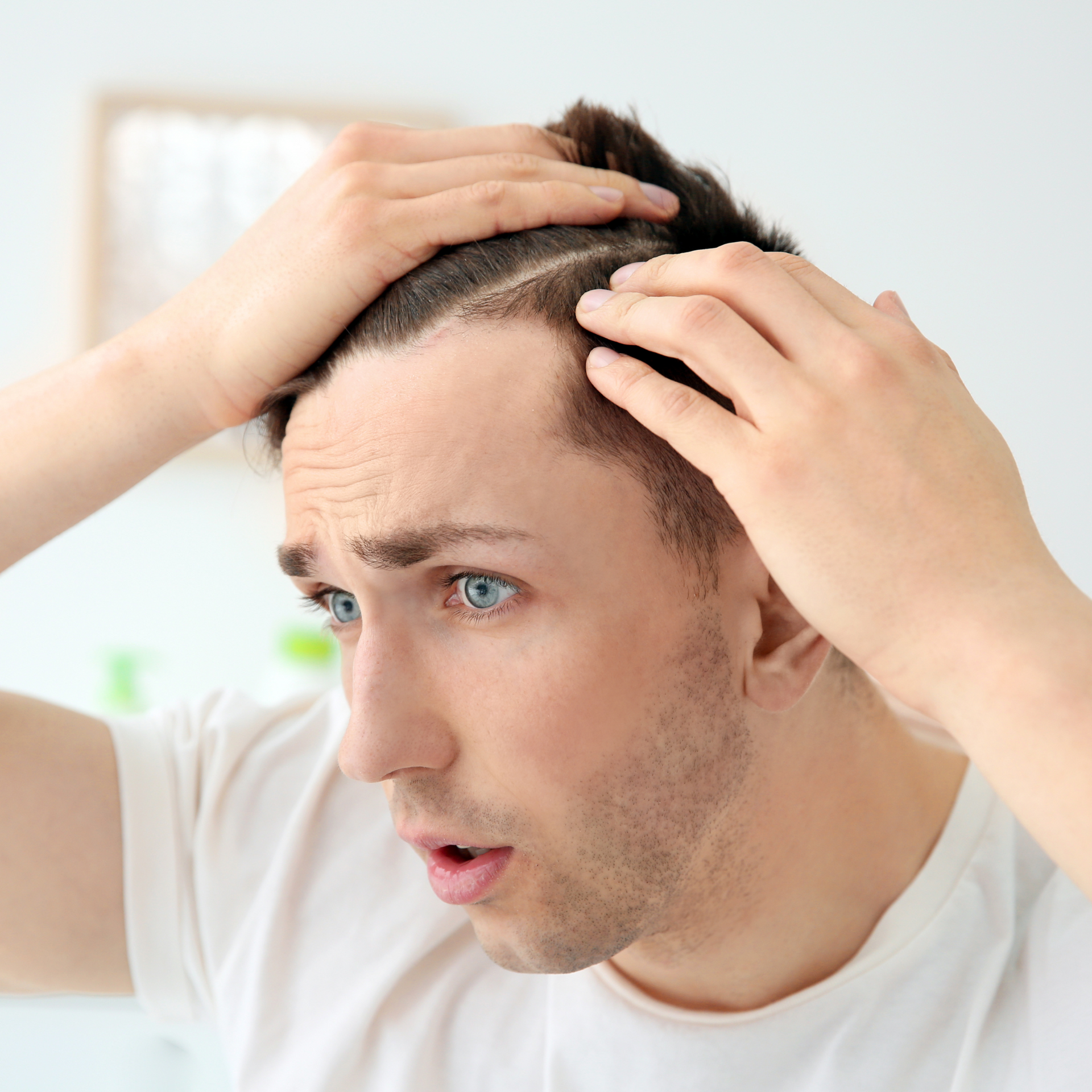 A man in a white shirt is holding his head and looking at his hair.