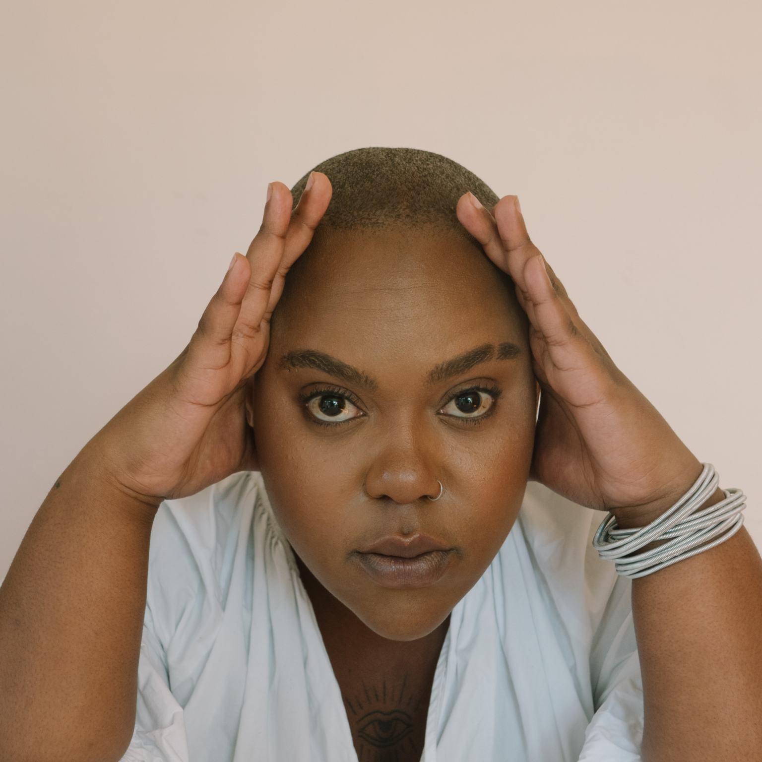 A woman with her hands on her head looks at the camera