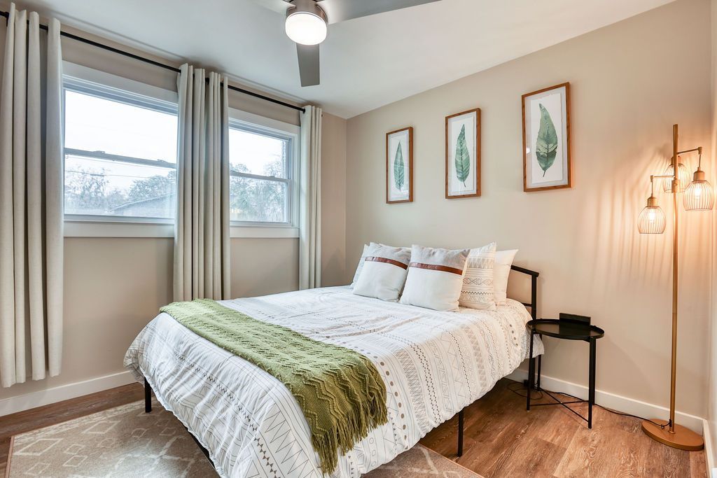 Bedroom with bed, windows, artwork, and floor lamp. White and green color scheme.