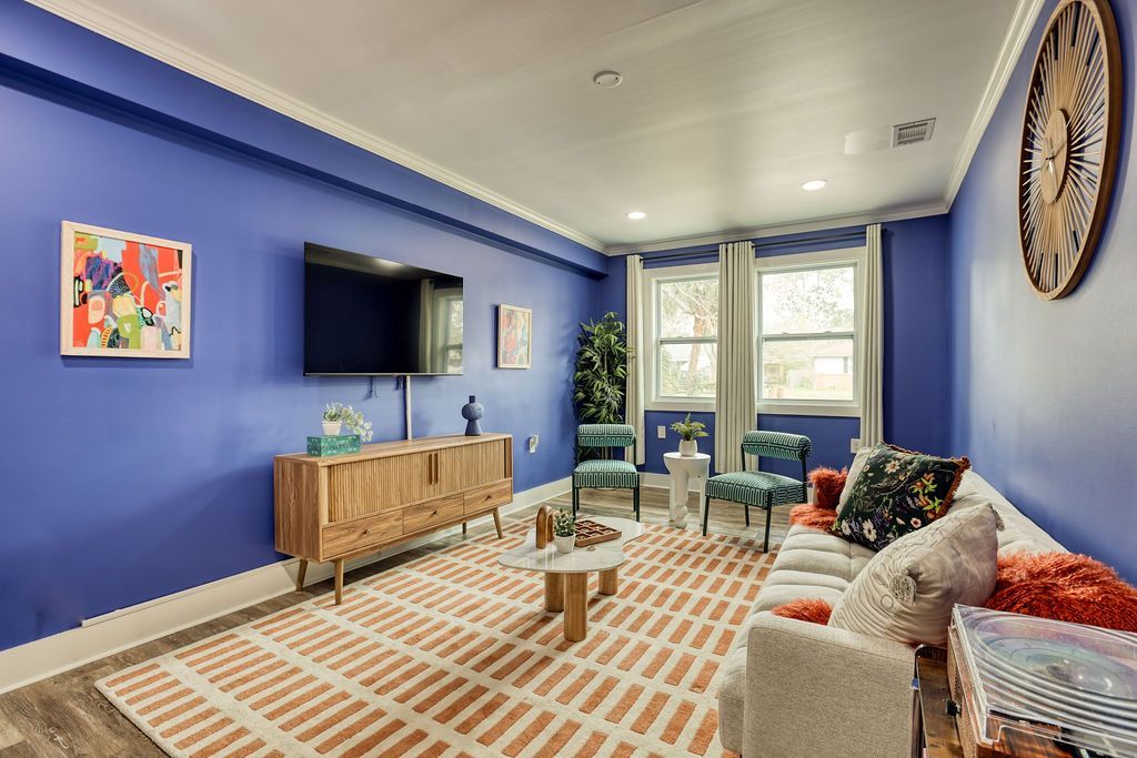 Living room with blue walls, white trim, wood TV stand, and orange patterned rug.