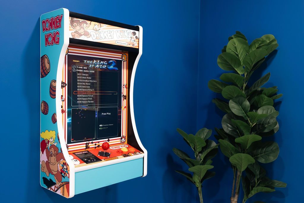 Light blue Donkey Kong arcade game mounted on a blue wall, next to a potted plant.