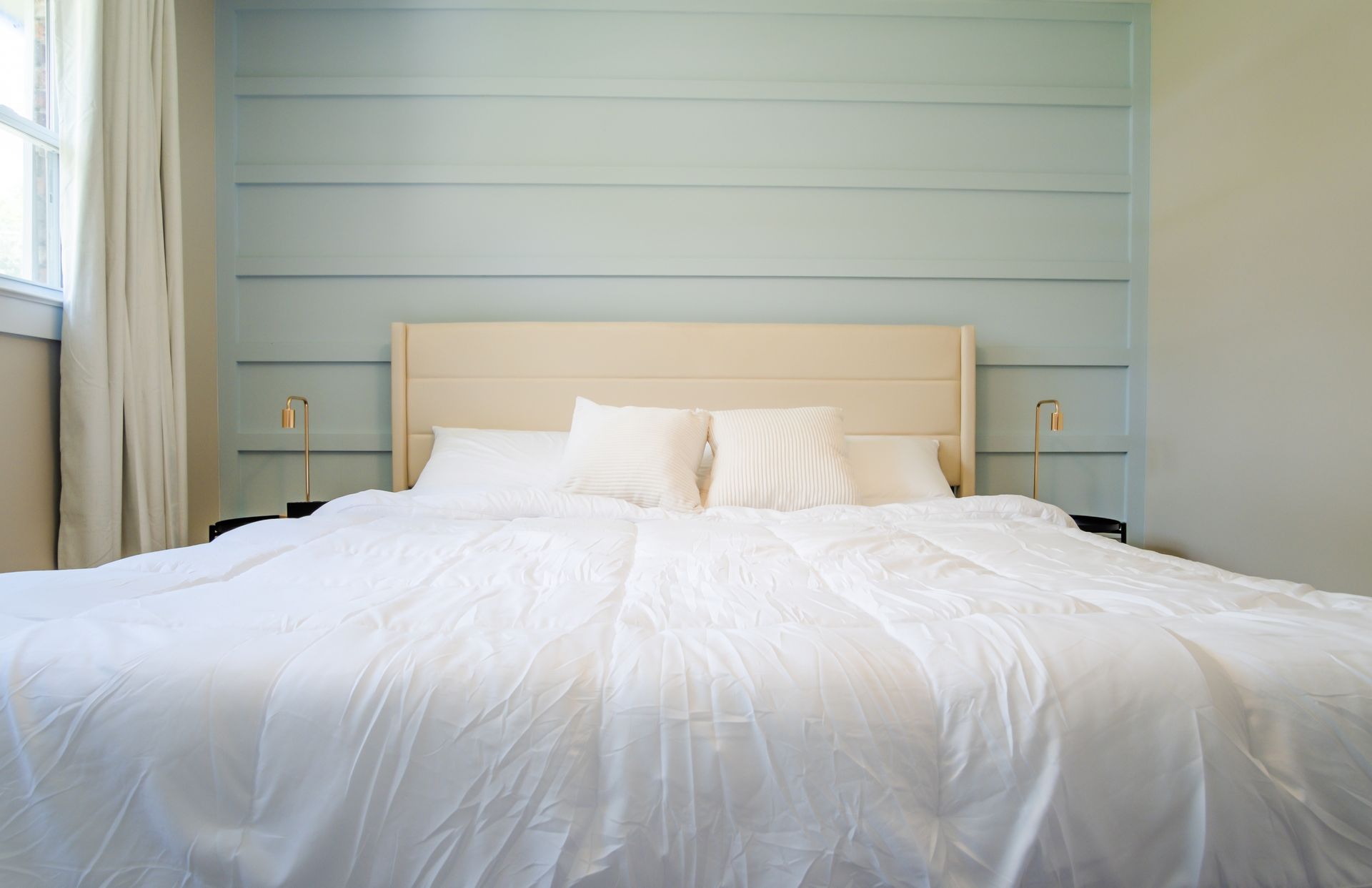 Bedroom with light blue paneled accent wall behind a bed with white bedding.