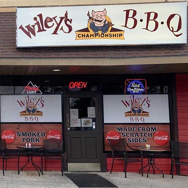 Wiley's BBQ restaurant exterior with a pig logo, red and white signage, and outdoor seating.