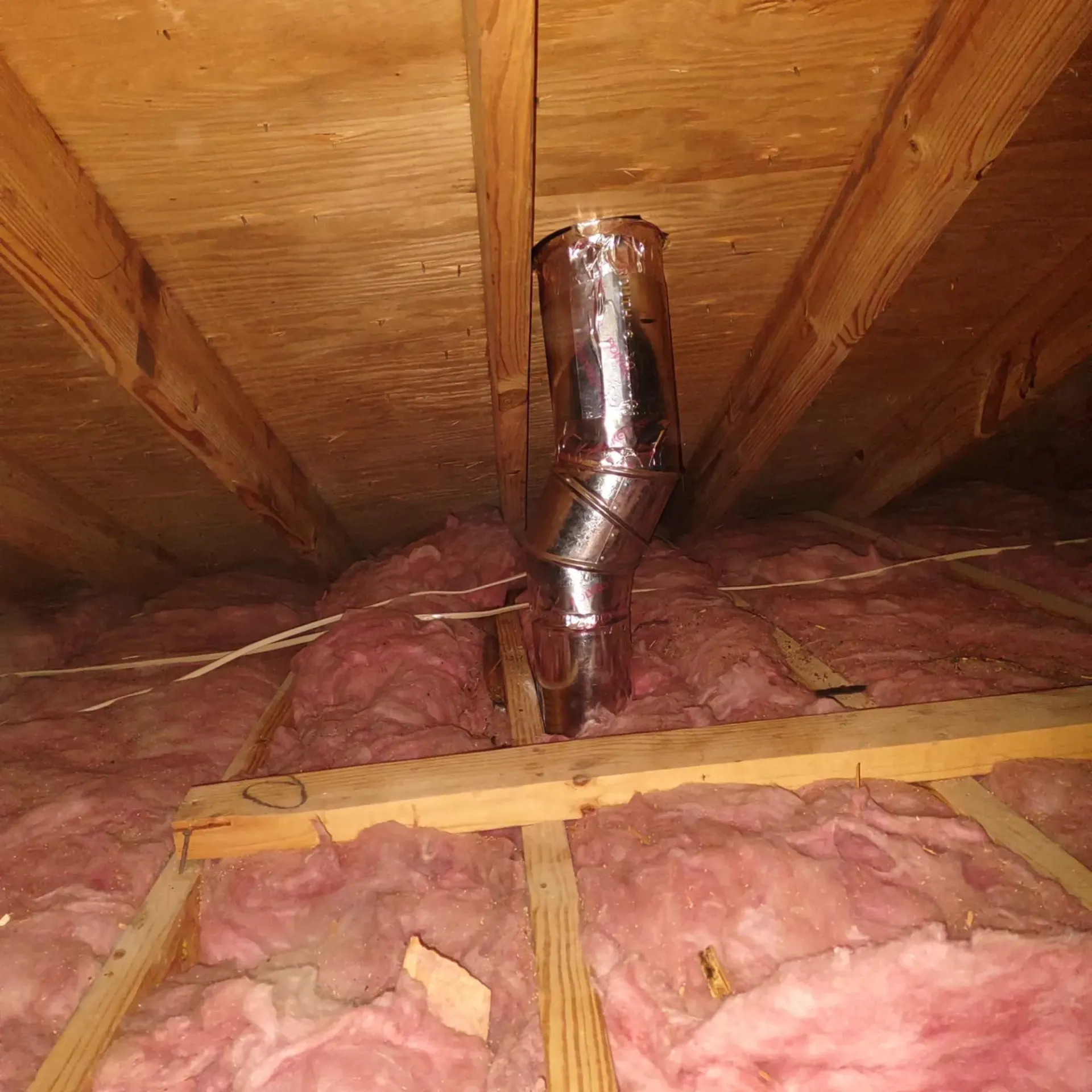 A metal pipe is hanging from the ceiling of an attic.