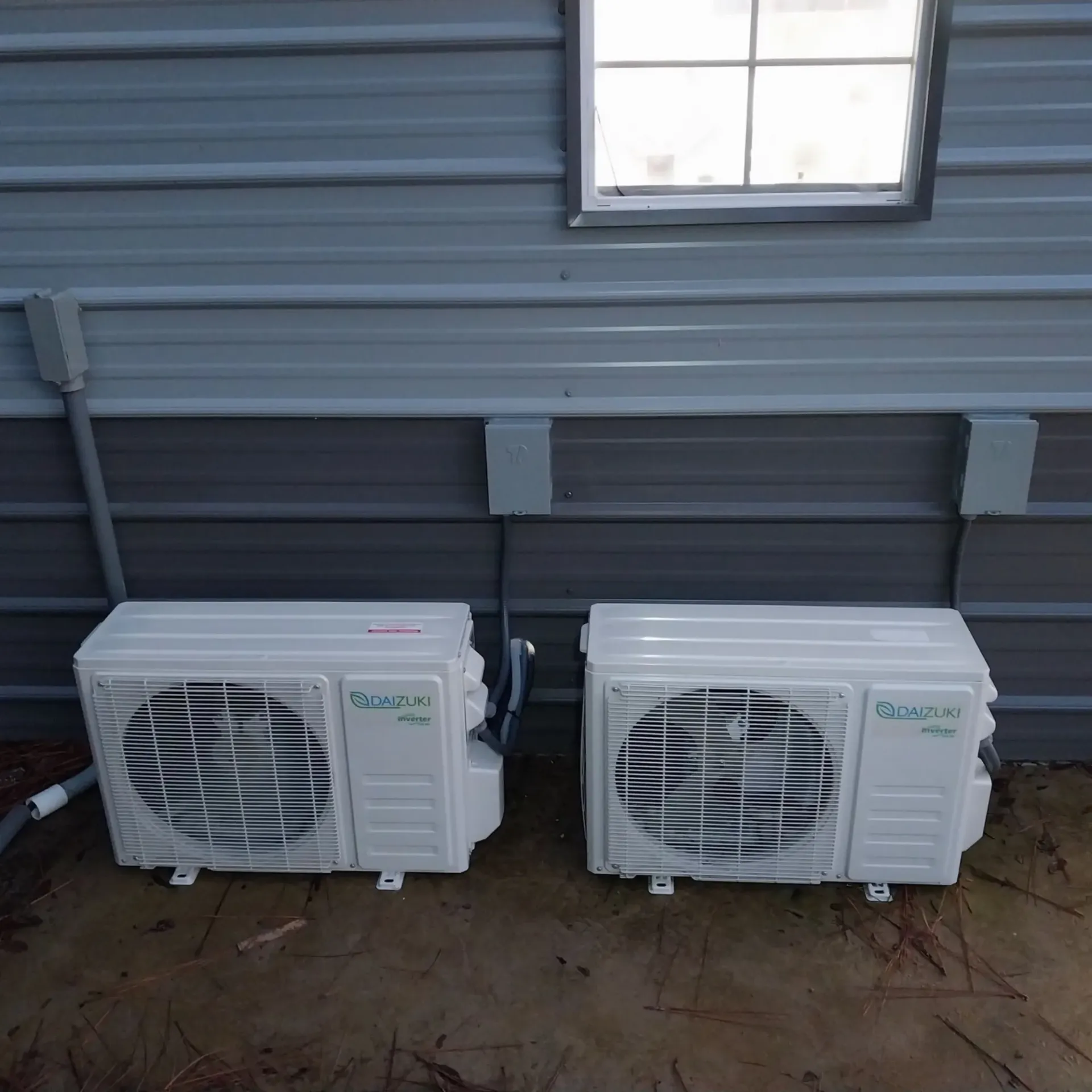Two air conditioners are mounted on the side of a building next to a window.