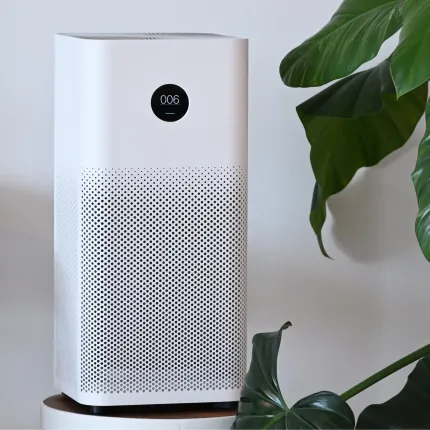 A white air purifier is sitting next to a plant.