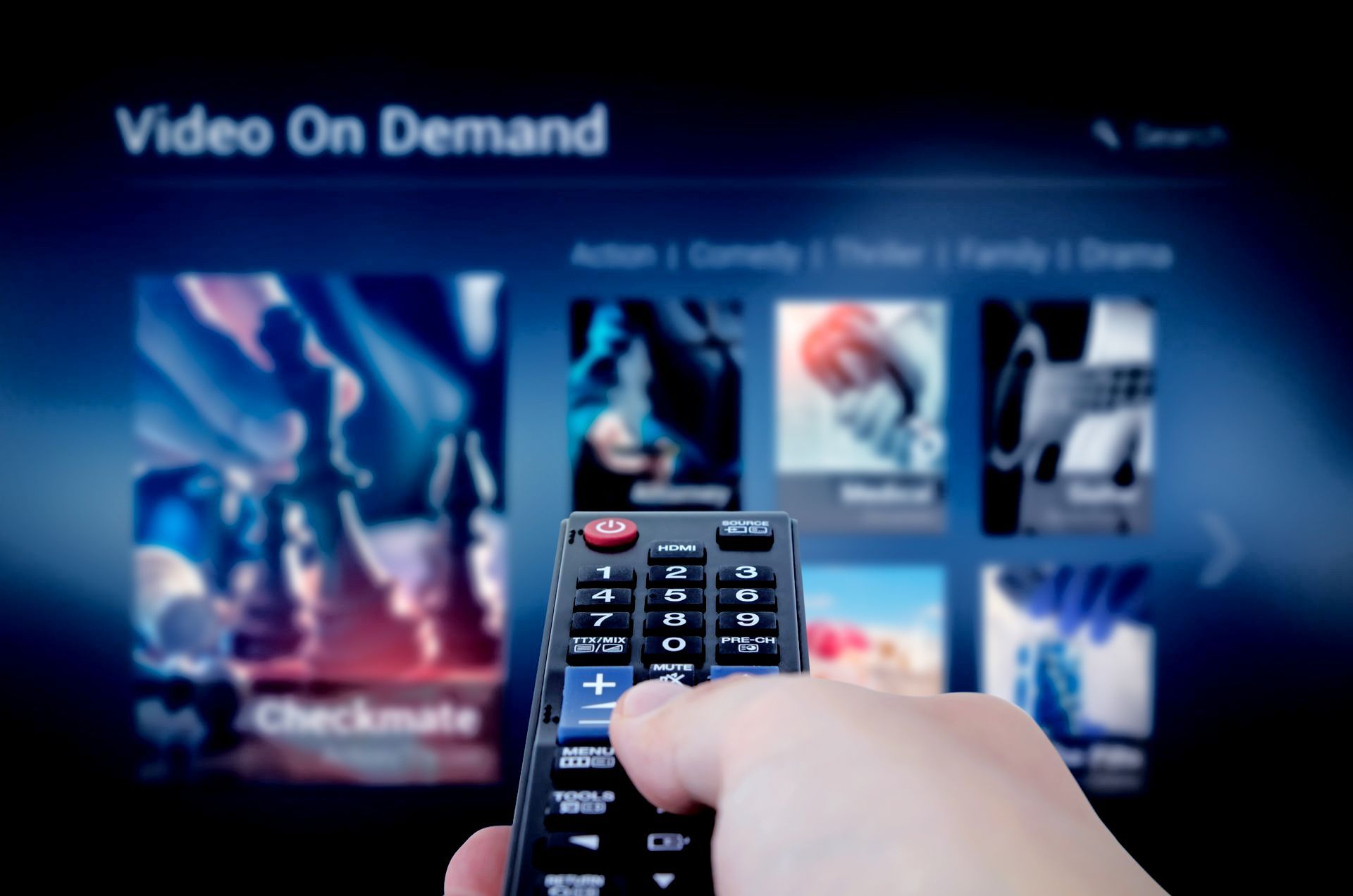 Hand holding TV remote in front of a video-on-demand menu on a television screen