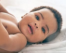 Baby lying on a white blanket, looking at the camera with a gentle smile.