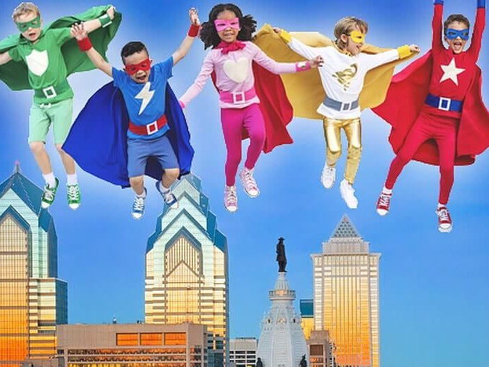 Five colorful superheroes jumping above a city skyline under a blue sky
