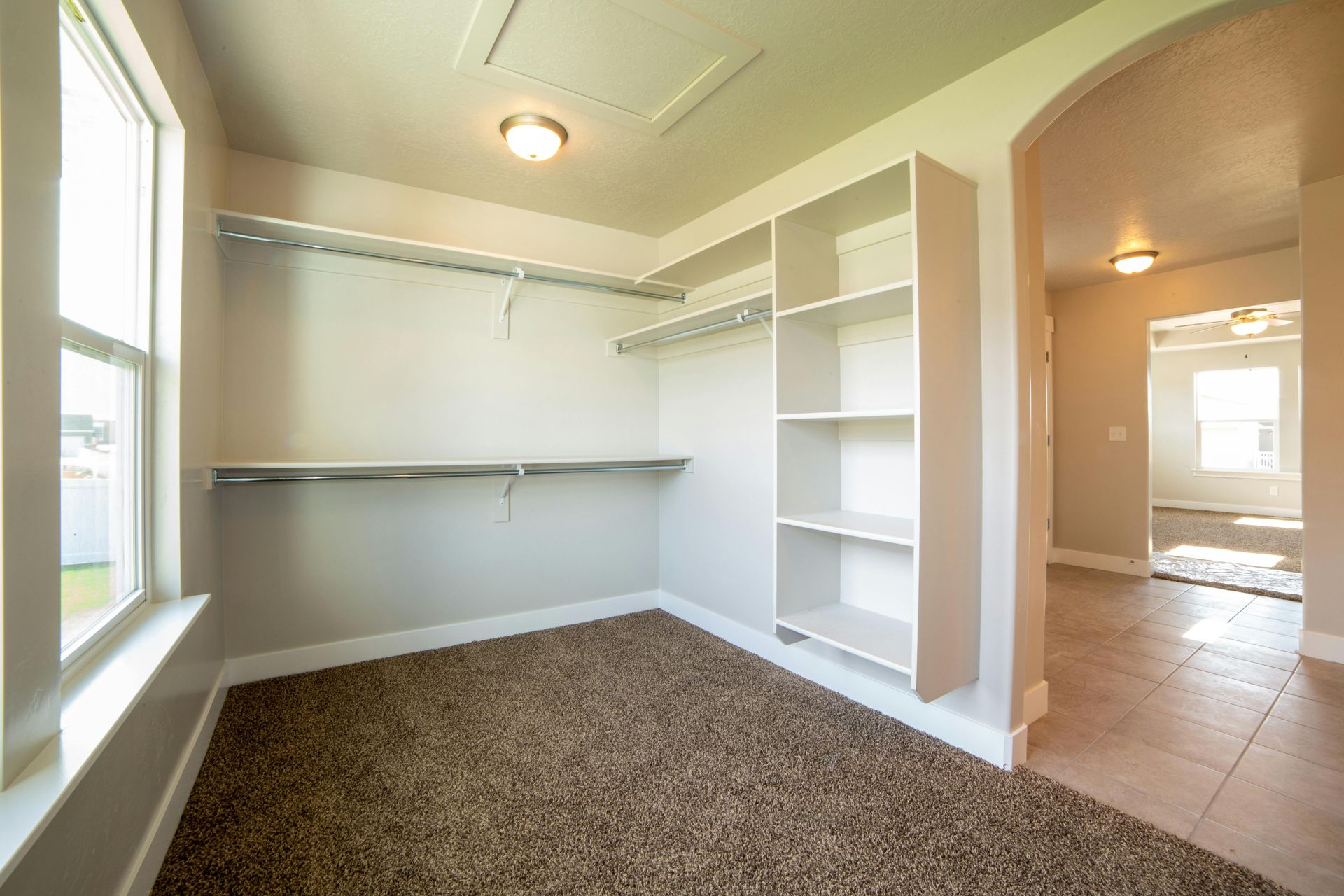 Empty walk-in closet with shelves, hanging rods, and carpet flooring. An arched doorway leads to another room.